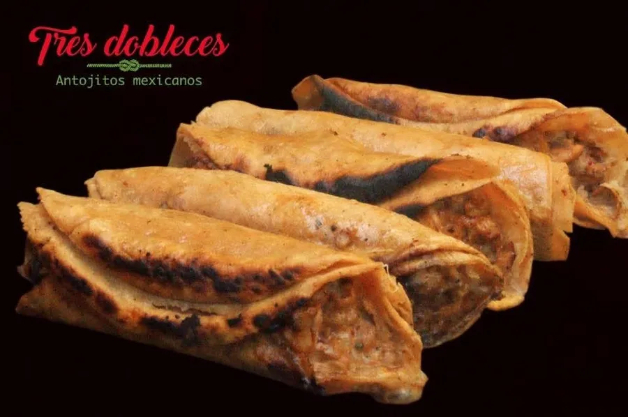 Cuatro tacos dorados con queso sobre fondo negro