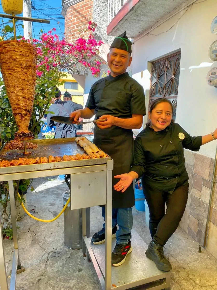 El puesto de Taquería Tres Dobleces: dos personas del equipo junto al trompo de pastor y la plancha con tacos dorados