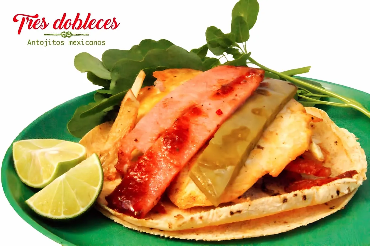 Taco de Taquería Tres Dobleces en plato verde, con chuleta, queso, papas y limones